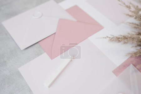Top view of composition of colorful sheets of paper of different sizes, white and pink envelopes sealed with wax, white sealing wax and dried twigs of pampas grass on grey background. Handmade craft. Poster 623376146