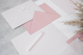 Top view of composition of colorful sheets of paper of different sizes, white and pink envelopes sealed with wax, white sealing wax and dried twigs of pampas grass on grey background. Handmade craft. Poster #623376146