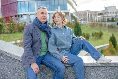 Photo for Nice, lovely, smiling mature man and woman in jeans outfit sit on stone railing against university building. Vacation and spend time together. Father and daughter, father day or university entrance - Royalty Free Image
