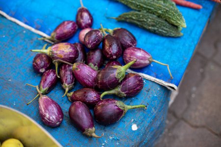 Téléchargez les photos : Quantité d'aubergines pourpres, petites et ovales empilées sur une nappe bleue sur le marché de Goa. Brinjals sains couchés sur la table près d'autres légumes et la vente au négoce en Inde. - en image libre de droit