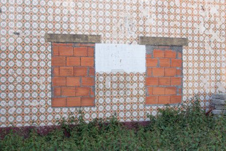 Ancienne maison abandonnée dans la campagne portugaise, avec des fenêtres en briques et des tuiles portugaises traditionnelles sur le mur.