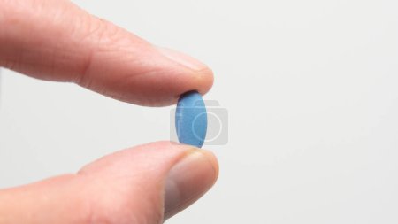 Blaue Pille gegen Impotenz oder erektile Dysfunktion. Hand hält Pille zwischen Finger und Daumen.
