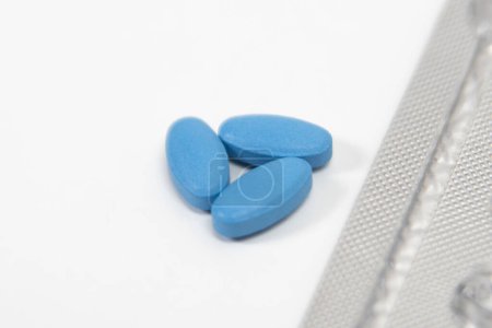 Blaue Pillen gegen Impotenz oder erektile Dysfunktion auf einem weißen Tisch mit Folienverpackung