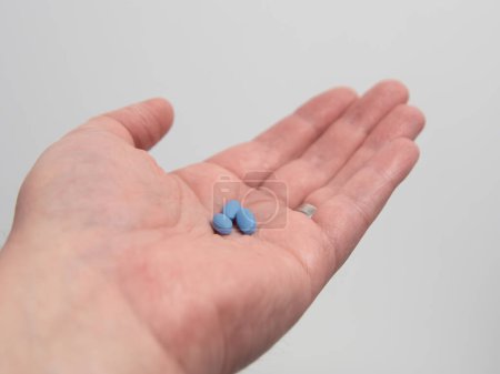Hand hält blaue Pillen zur Behandlung von Impotenz oder erektiler Dysfunktion
