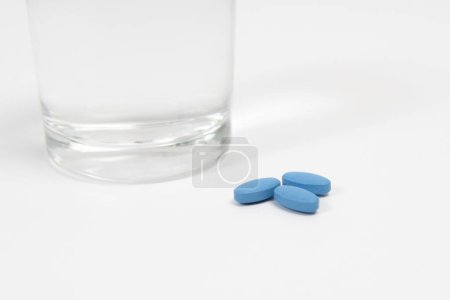 Blaue Rechnungen zur Behandlung der erektilen Dysfunktion auf einem weißen Tisch mit einem Glas Wasser. Nahaufnahme.