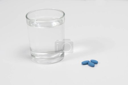 Blaue Rechnungen zur Behandlung der erektilen Dysfunktion auf einem weißen Tisch mit einem Glas Wasser