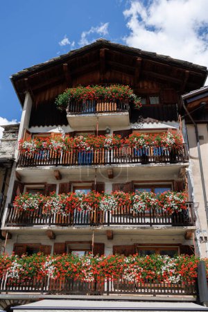 Téléchargez les photos : Vue de la façade extérieure d'une maison de montagne avec des fleurs rouges et blanches sur tous les balcons, Italie - en image libre de droit