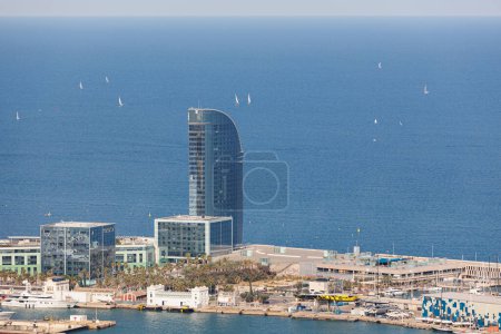 View of a Skyscraper with Mirrored Windows near the Port of Barcelona, and a Multitude of Sailboats in the Sea Ahead, Spain.
