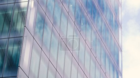 Téléchargez les photos : Extérieur du bureau d'entreprise avec des fenêtres en verre réfléchissantes, capturant la lumière du soleil et un ciel lumineux. - en image libre de droit
