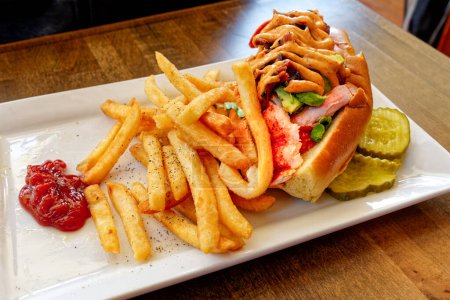 Lobster sandwich with avocado and southwest mayo on a white plate with french fries and ketchup