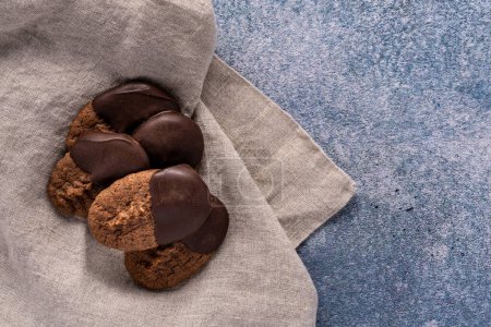Téléchargez les photos : Biscuits spritz au chocolat trempés dans du chocolat posé sur une serviette de lin assise sur un fond bleu marbré - en image libre de droit