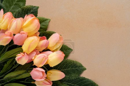 Téléchargez les photos : Tulipes en soie rose et jaune doux avec des feuilles vertes sur un fond jaune pâle marbré avec espace de copie - en image libre de droit
