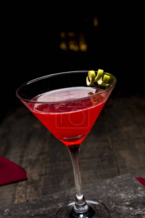 Foto de Cóctel rojo en un vaso de martini sobre una mesa de madera sobre un fondo negro - Imagen libre de derechos