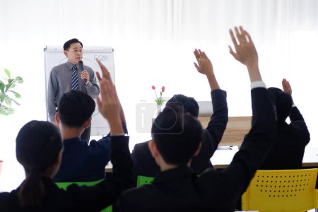 Photo for Senior Asian Lecturer is lecturing about business and stock market topics and business people are having a seminar and raising hands agree with teacher in the economics class in meeting room - Royalty Free Image
