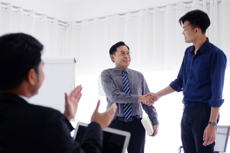 Photo for Senior Asian Lecturer is shaking hand with young businessman for congratulate on the success of his work and business. Stock market for people in the economics class at meeting or seminar room - Royalty Free Image