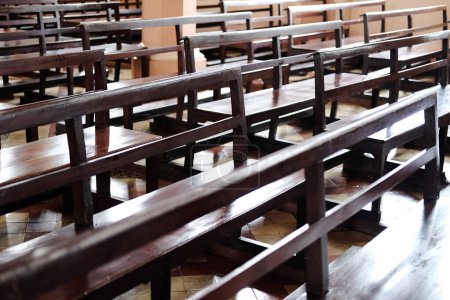 Lange Holzstühle zum Sitzen und Segensgebet in christlichen Kirchen. Reihen von Kirchenbänken im Sonnenlicht