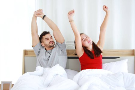 Smiling Caucasian lover Couple wake up and stretch lazily on the bed in the morning on holiday at home. Lifestyle and relationship of married life Concept