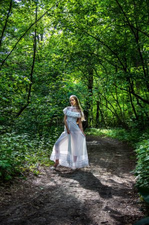 Téléchargez les photos : Fille dans une longue robe blanche transparente dans la forêt aux rayons du soleil. Concentration douce. - en image libre de droit