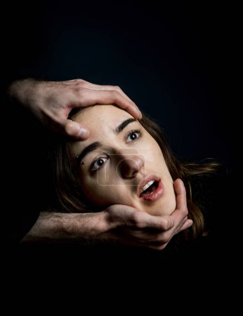 Men's hands hold a woman's head on a black background. Fear, suffering.