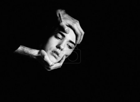 Men's hands hold a woman's head on a black background. Fear, suffering. Black and white portrait.