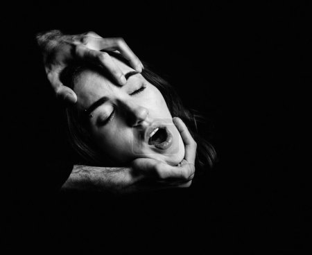 Männerhände halten den Kopf einer Frau auf schwarzem Hintergrund. Angst, Leid. Schwarz-Weiß-Porträt.