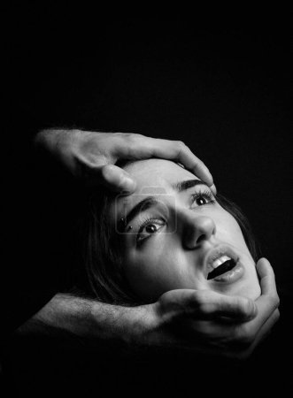 Men's hands hold a woman's head on a black background. Fear, suffering. Black and white portrait.