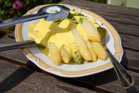 Asperges blanches fraîches sur une assiette avec sauce hollandaise et pinces d'asperges.