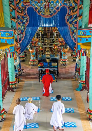 Téléchargez les photos : Ho Chi Minh Ville, Vietnam - 5 janvier. 2015 : Salle intérieure de l'église de Cao Dai (Caodaïsme) avec prêtre en prière et croyants en robes blanches, autel coloré - en image libre de droit