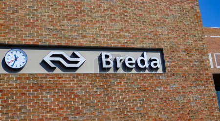 Foto de Breda, Países Bajos - 30 de agosto. 2023: Pared de ladrillo rojo con letras de logotipo de la estación de tren holandés de la ciudad y reloj - Imagen libre de derechos