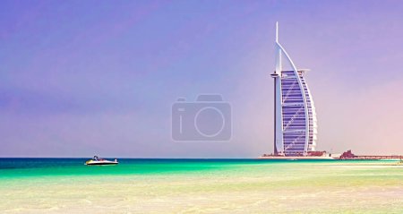 Foto de Dubai (Burj Al Arab), VAE - 9 de marzo. 2019: Torre árabe del hotel costero de lujo en la playa solitaria del paraíso de la arena blanca, océano turquesa, un yate del barco a motor - Imagen libre de derechos