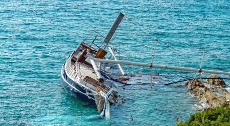 Photo for Rocky coast with stranded damaged sailboat with broken mast in French Mediterranean sea after storm  (focus on boat) - Royalty Free Image