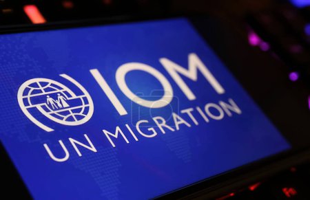 Téléchargez les photos : Viersen, Allemagne - 9 janvier. 2024 : Ecran Smartphone avec lettrage logo de l'agence des Nations Unies Organisation internationale pour les migrations OIM sur clavier d'ordinateur - en image libre de droit