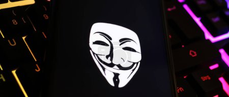 Foto de Viersen, Alemania - 9 de enero. 2024: Pantalla de teléfono inteligente con símbolo de máscara anónima en el teclado del ordenador como ciberataque y concepto de piratería - Imagen libre de derechos