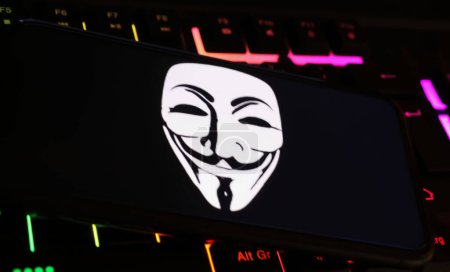 Foto de Viersen, Alemania - 9 de enero. 2024: Pantalla de teléfono inteligente con símbolo de máscara anónima en el teclado del ordenador como ciberataque y concepto de piratería - Imagen libre de derechos