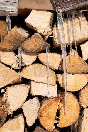 Hintergrund und Struktur von gestapeltem Brennholz im Winter. Eiszapfen hängen von oben