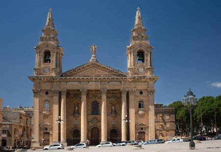 Photo for N front of the parish church "St. Publius" in Malta, a man stands and looks towards the church. The 18th century church is made of limestone. Cars are parked in front of the church. - Royalty Free Image