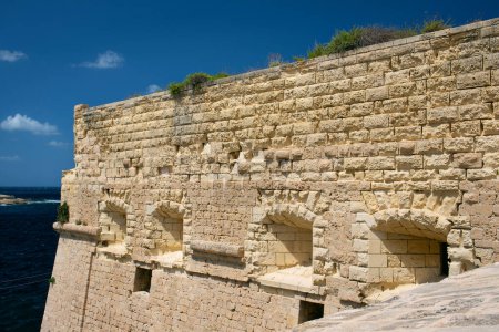 Foto de Detalle del muro exterior del Fuerte de San Elmo en La Valeta, Malta. Las piedras erosionadas y las lagunas son claramente visibles. En el fondo cielo azul. - Imagen libre de derechos
