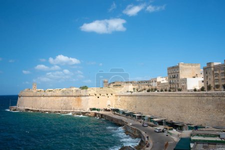 Foto de El Muro de Fort St. Elmo en Malta en La Valeta. En el fondo el cielo azul y las nubes. En primer plano el mar y la playa. - Imagen libre de derechos