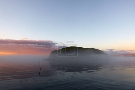 Téléchargez les photos : Petite île de Lille Kamoya tard dans la soirée d'août juste à l'extérieur du village de pêcheurs de Kamyvr avec soleil de minuit et brouillard marin. - en image libre de droit