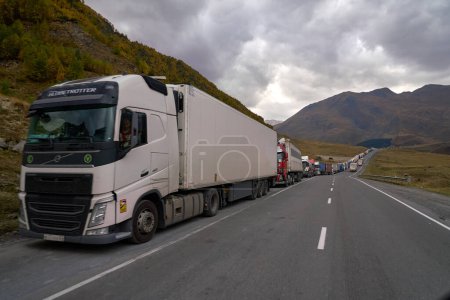 Photo for Kazbegi, Georgia - October 3, 2022: Several kilometres long line of Trucks by the side of the Georgian military highway near Kazbegi waiting for crossing to Russia at ZemoLarsi / VerkhnyLars border crossing further up on the road. - Royalty Free Image