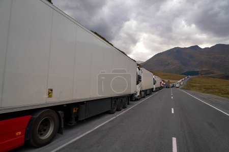 Photo for Kazbegi, Georgia - October 3, 2022: Several kilometres long line of Trucks by the side of the Georgian military highway near Kazbegi waiting for crossing to Russia at ZemoLarsi / VerkhnyLars border crossing further up on the road. - Royalty Free Image