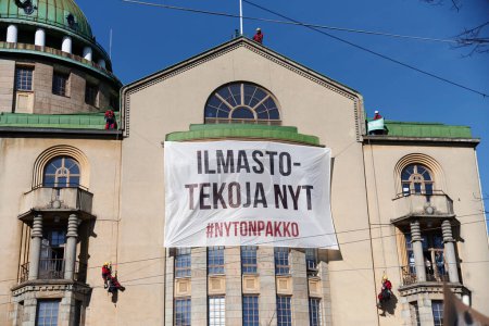 Photo for Helsinki, Finland - April 6, 2019: Greenpeace activists climb wall of the New Student House and place Climate action now (Ilmastotekoja nyt in Finnish) banner in the center of Helsinki. - Royalty Free Image