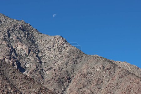 Téléchargez les photos : Une lune d'automne diurne sourit de façon ludique en survolant les rochers de la montagne San Ysidro depuis le désert de la vallée de Borrego. - en image libre de droit