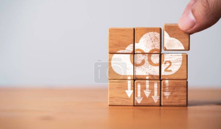 Hand assembly CO2 reducing icon on wooden block cube for decrease CO2 or carbon dioxide emission ,carbon footprint and carbon credit to limit global warming from climate change concept. 