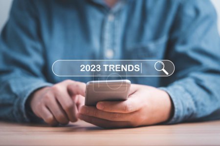 Geschäftsmann mit Smartphone zur Eingabe von Schlüsselwörtern der 2023 Trends in der Infografik Suche Werkzeugleiste für Marketing-Monitor und Geschäftsplanung Änderungskonzept