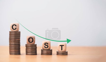 Photo for Cost wording on decreasing coins stacking with down arrow for cost reduction concept which effect to product cost , profit , inflation and economy recession concept. - Royalty Free Image