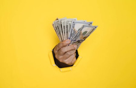 Téléchargez les photos : Homme d'affaires tenant billet de billet de dollar à partir de papier perforé jaune pour l'argent et le paiement USD, l'inflation et la notation d'intérêt concept croissant. - en image libre de droit