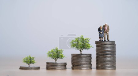 Couple of old man and woman standing on increasing coins stacking with glowing tree for money saving and investment to get interest and dividend, retirement concept.