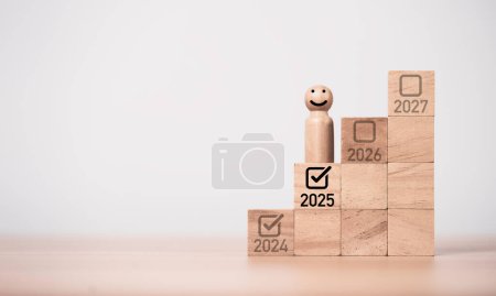 Wooden miniature figure smiling and standing on 2025 and correct tick mark for start and preparation of merry Christmas and happy new year concept.