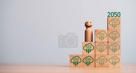 Miniaturfigur lächelt und steht auf CO2-Reduktion Symbol auf Holzblock Würfel für progressive der CO2-Gutschrift Fußabdruck für Kohlendioxid-Aufnahme, um die globale Erwärmung innerhalb 2050 Konzept zu begrenzen.